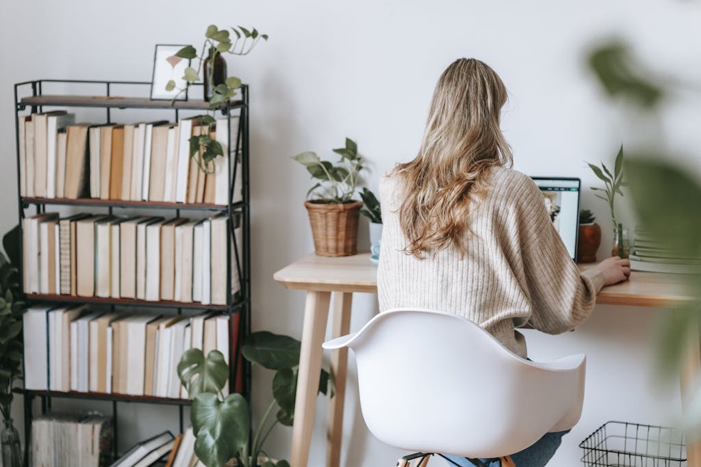 Unrecognizable freelancer working on laptop against bookcase at home